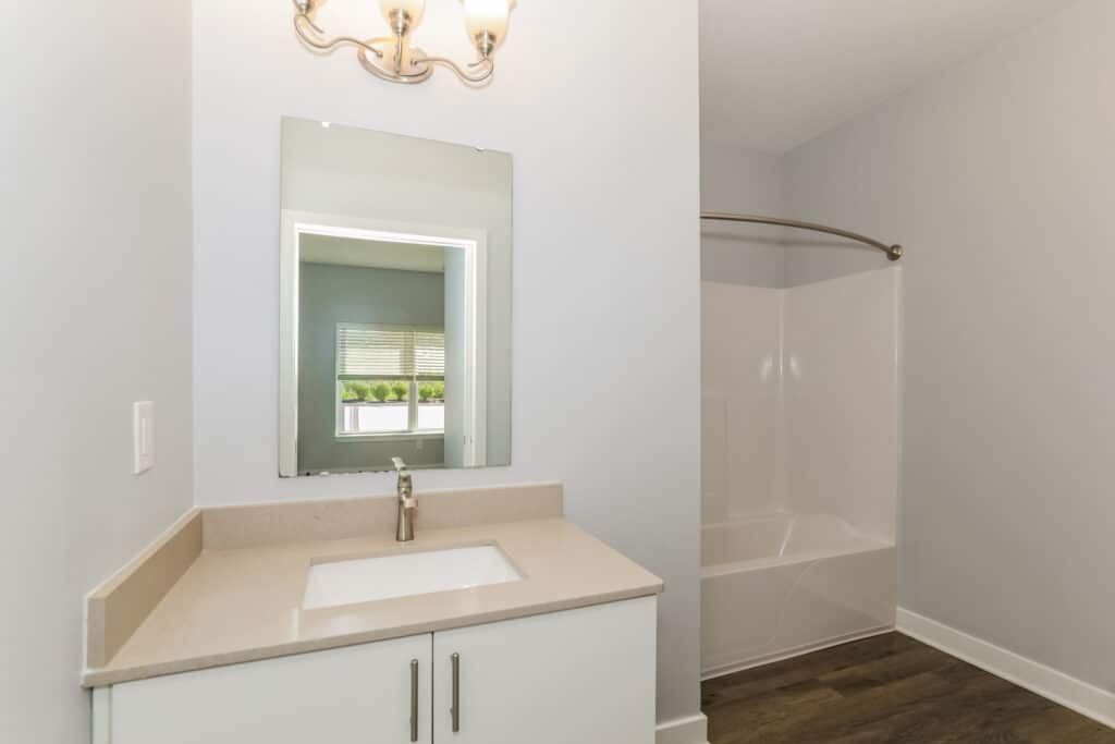 Modern bathroom with a single-sink vanity, wall mirror, light fixture, and a white bathtub with a curved shower rod on the right.