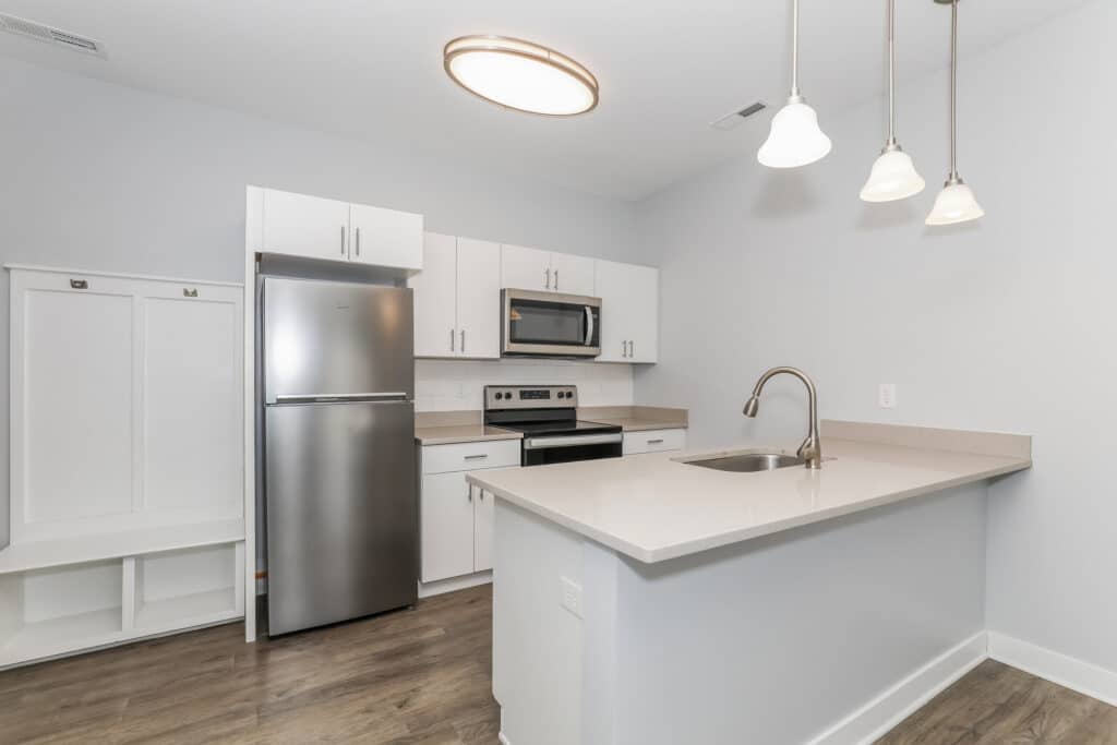 Modern kitchen with stainless steel appliances, white cabinets, an island with a sink, pendant lights, and wood flooring.