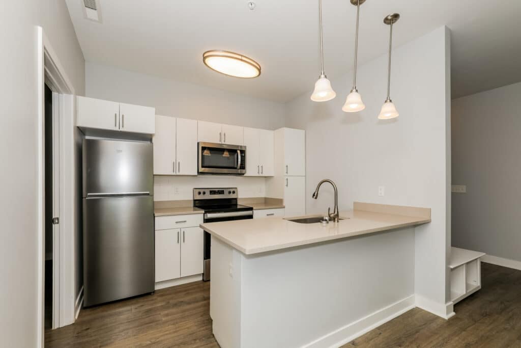 Modern kitchen with stainless steel appliances, white cabinets, a built-in microwave, a stove, and an island with sink under hanging pendant lights.