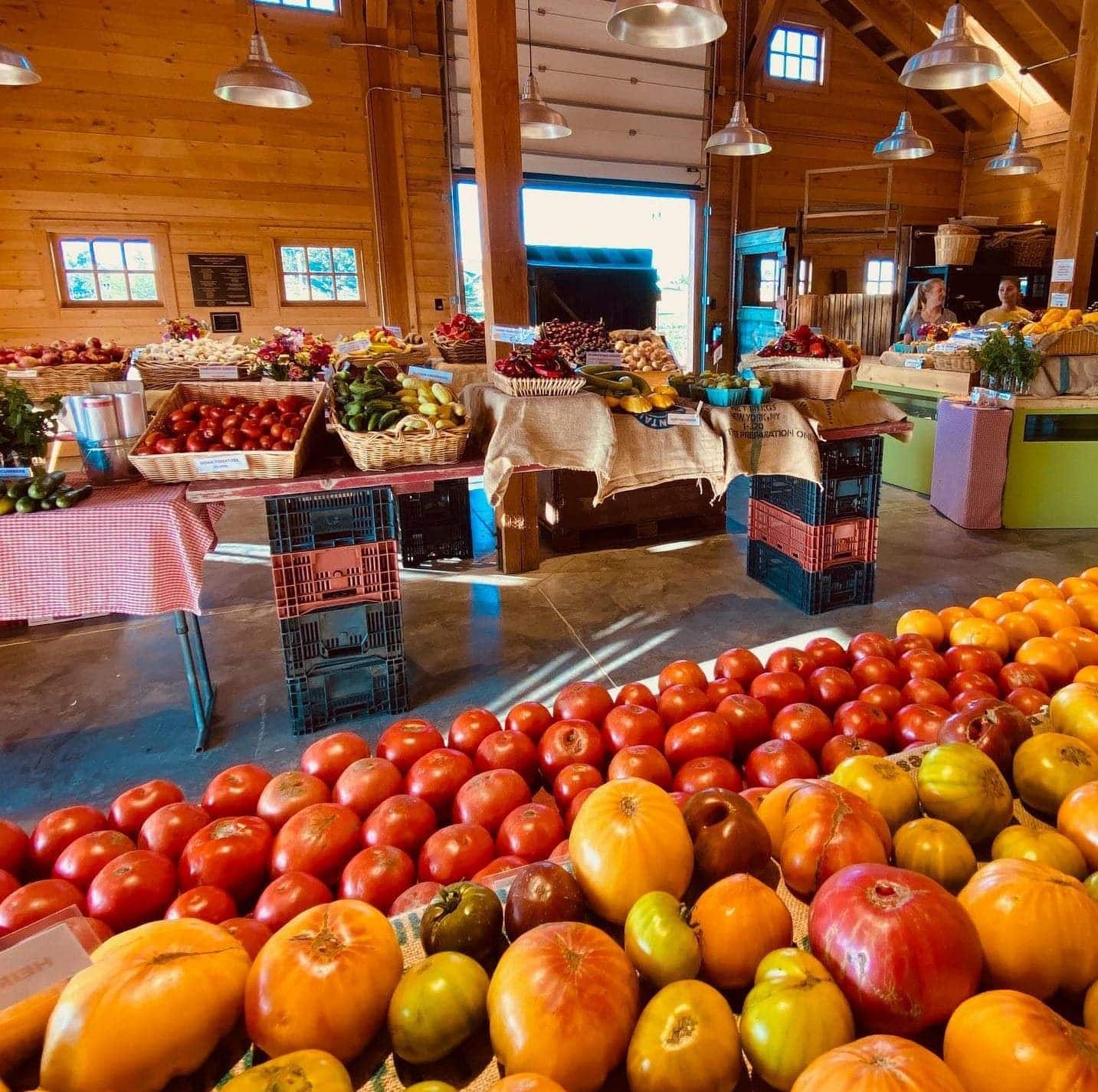 A variety of colorful tomatoes and other fresh produce are displayed on tables inside a rustic, wooden market building.